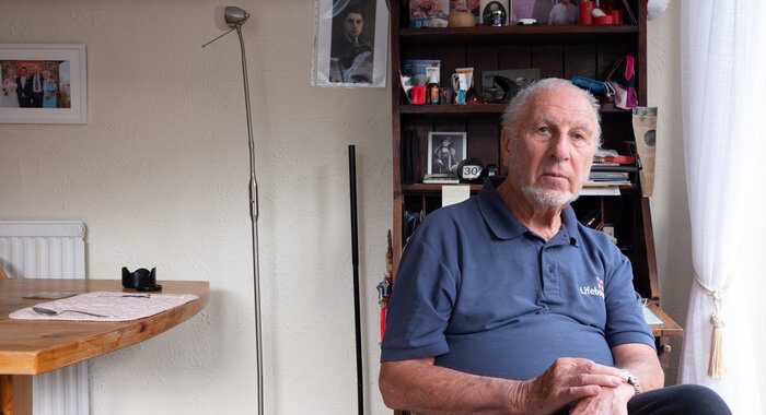 An older man at home sitting on a chair looking at the camera