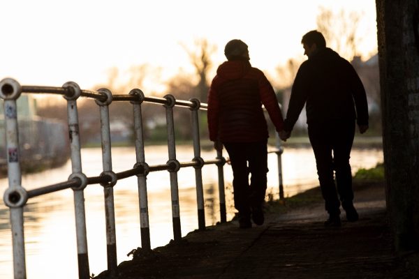 Two people walk along a canal path holding hands.