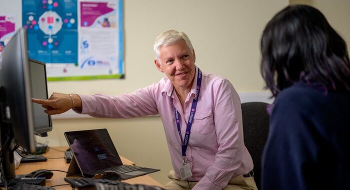 Two people in a clinic. One is smiling and pointing at a computer screen. The other person has their back to the camera and is also looking at the computer screen