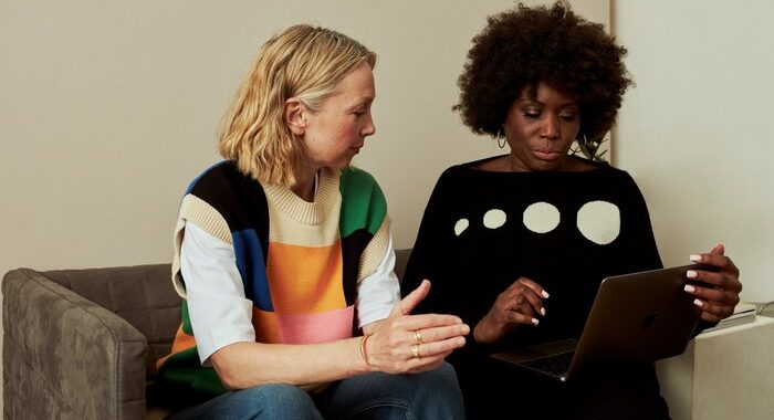 Two women sitting on a sofa looking at a laptop together