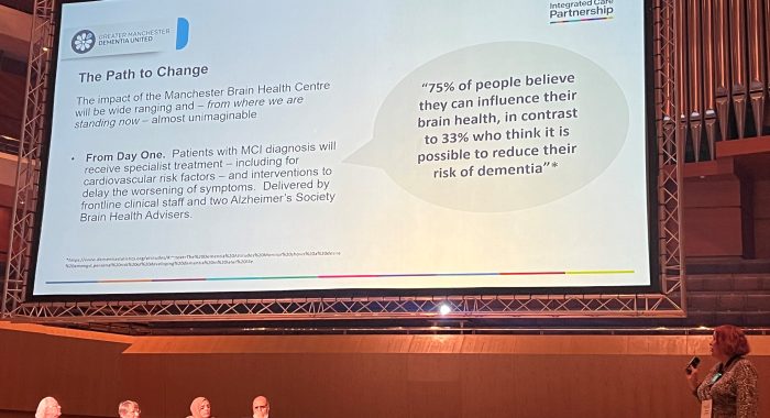 A photo at the 19th UK Dementia Congress featuring: Ruth Turner and Ann Booth (both DCERG), Sania Rehman (Team Sahara South Asian Project Greater Manchester), Masood Ahmed Qureshi (Expert by Experience, Team Sahara), Sarah Kirkland (Senior Project Manager, Dementia United) sitting on the stage and Andy Burnham, Mayor of Greater Manchester standing and speaking