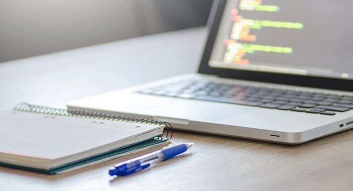 An open laptop, a pen and a notebook on a table